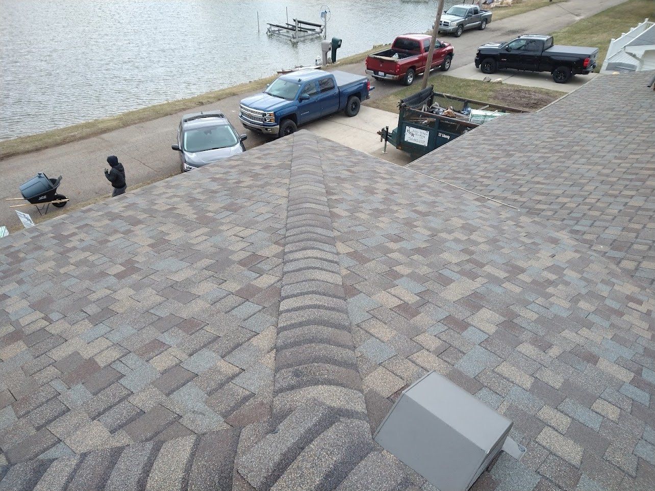 View from a roof, showing asphalt shingles and trucks parked by a lake.