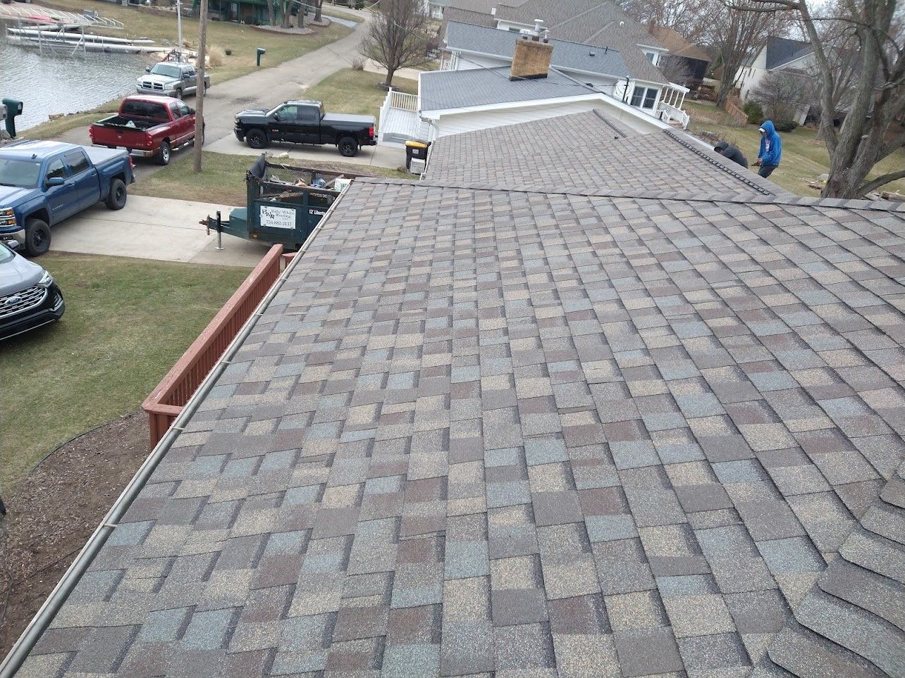View of a shingled roof with a lake and vehicles in the background.