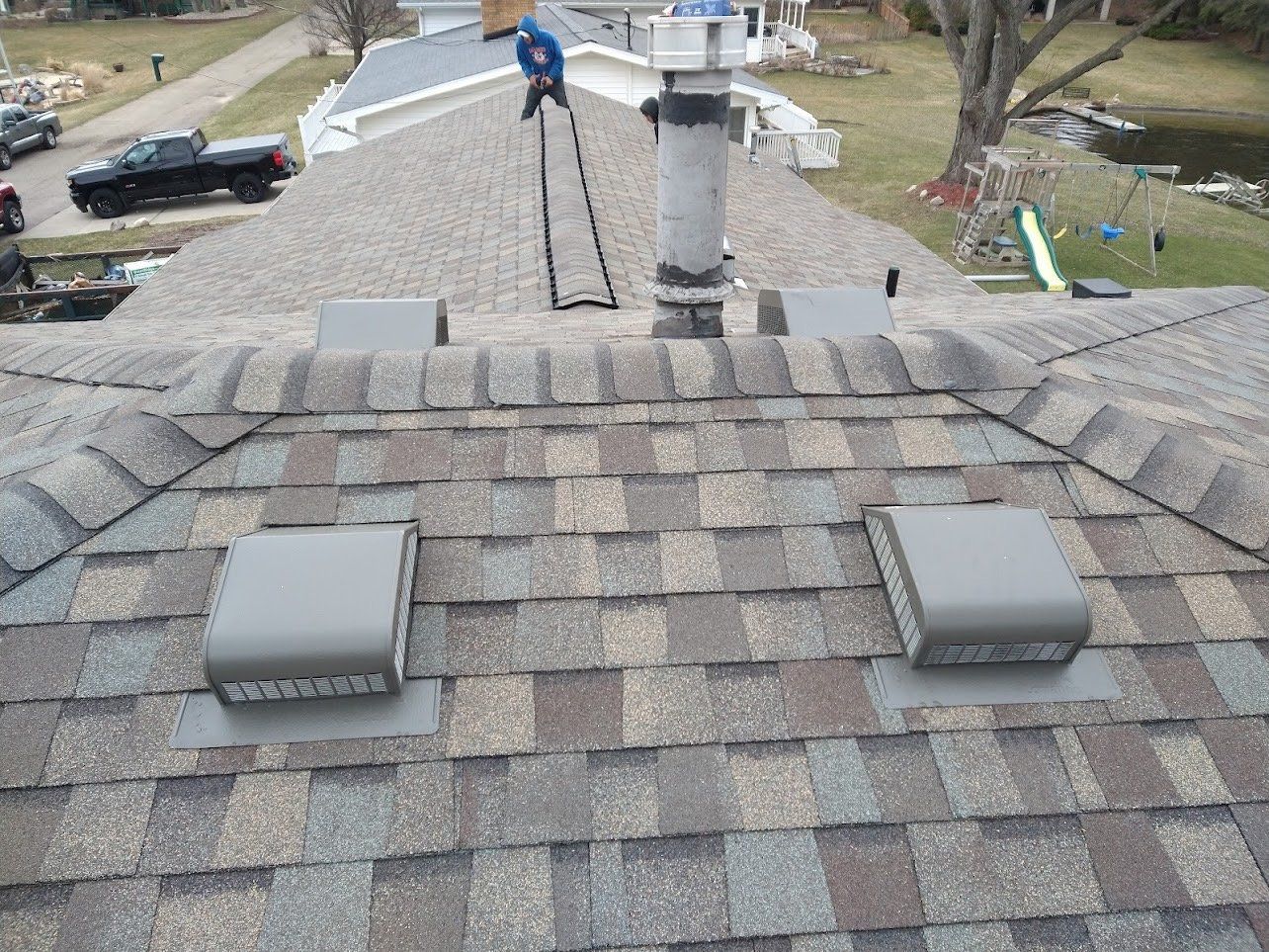 Gray shingle roof with two vents, a chimney, and a person working on top.