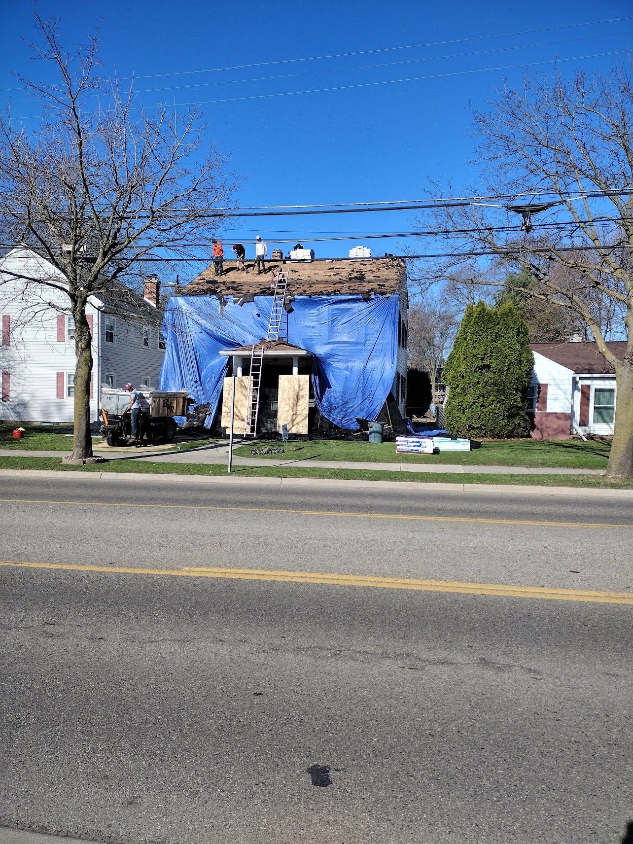 House covered in blue tarp, under construction; sunny day.