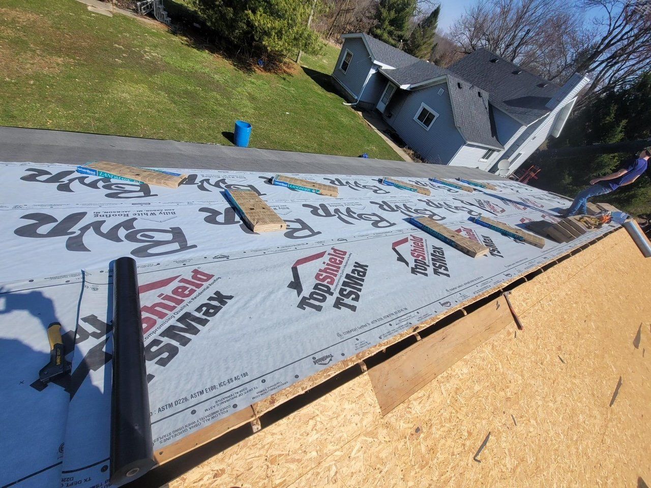 Roofers installing roofing material on a house, sunny day.