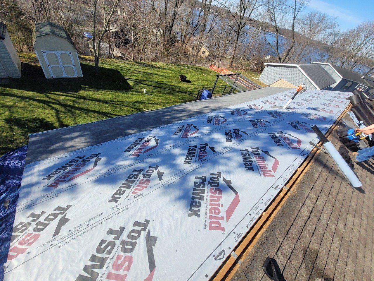Roof being worked on, with underlayment installed. Sheds and water in background.
