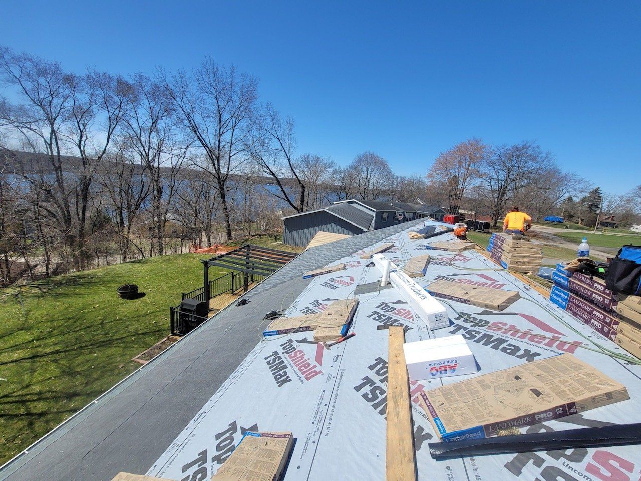 Roofing work in progress on a residential roof, overlooking a lake on a sunny day.