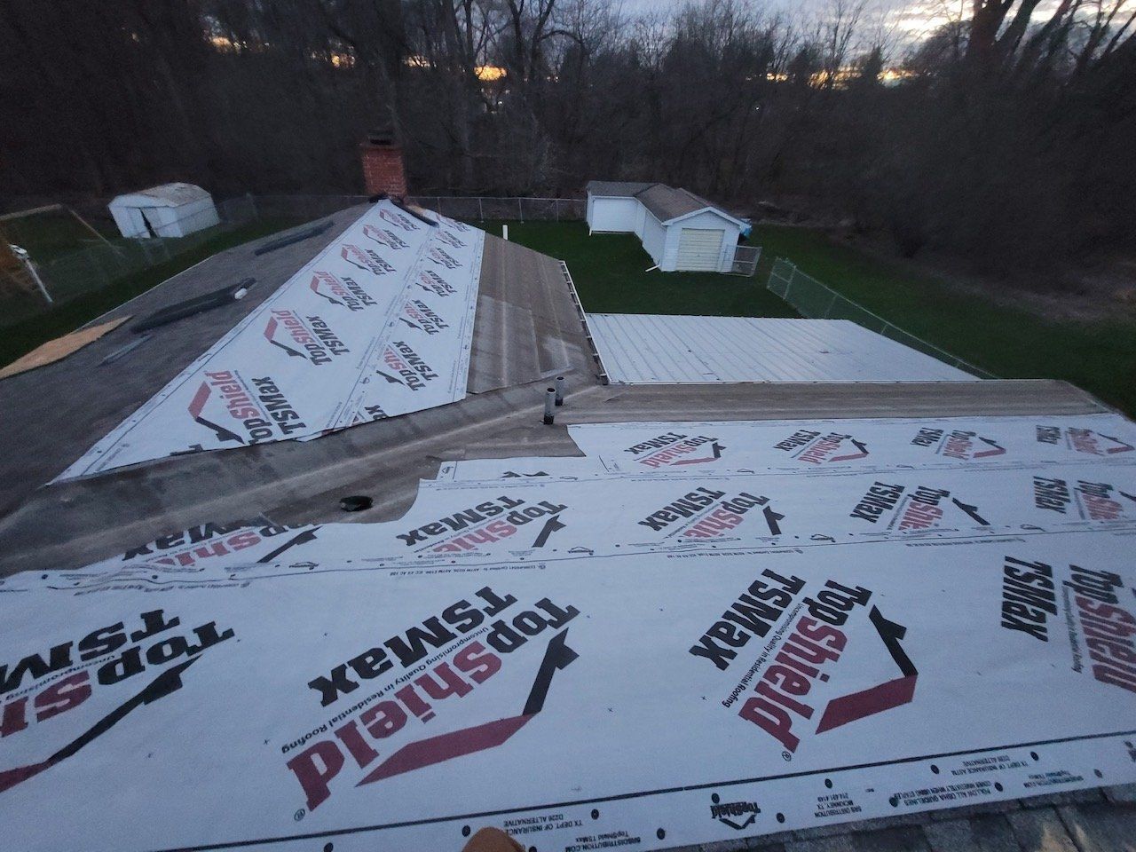 Roofing work in progress on a residential home with underlayment installed, a cloudy sky in the background.