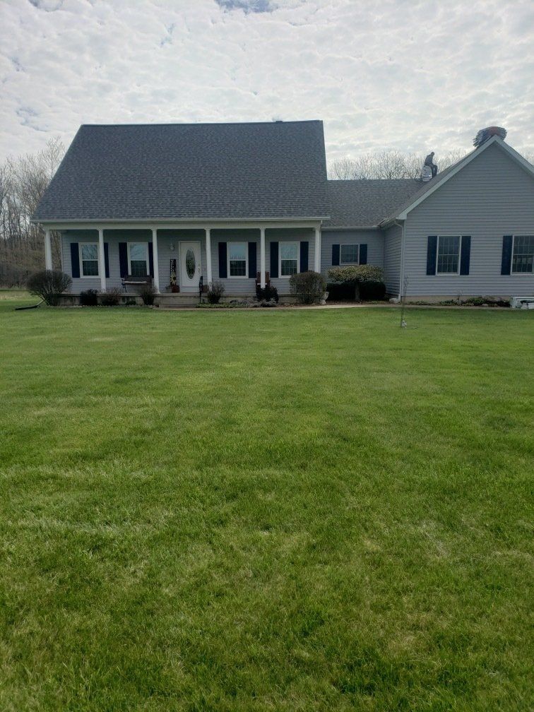 Gray house with a large green lawn under a cloudy sky.