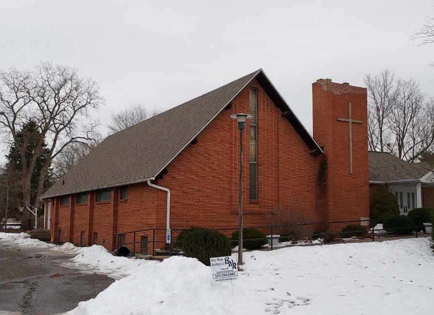 Red brick church with a cross on the side tower and snow on the ground.