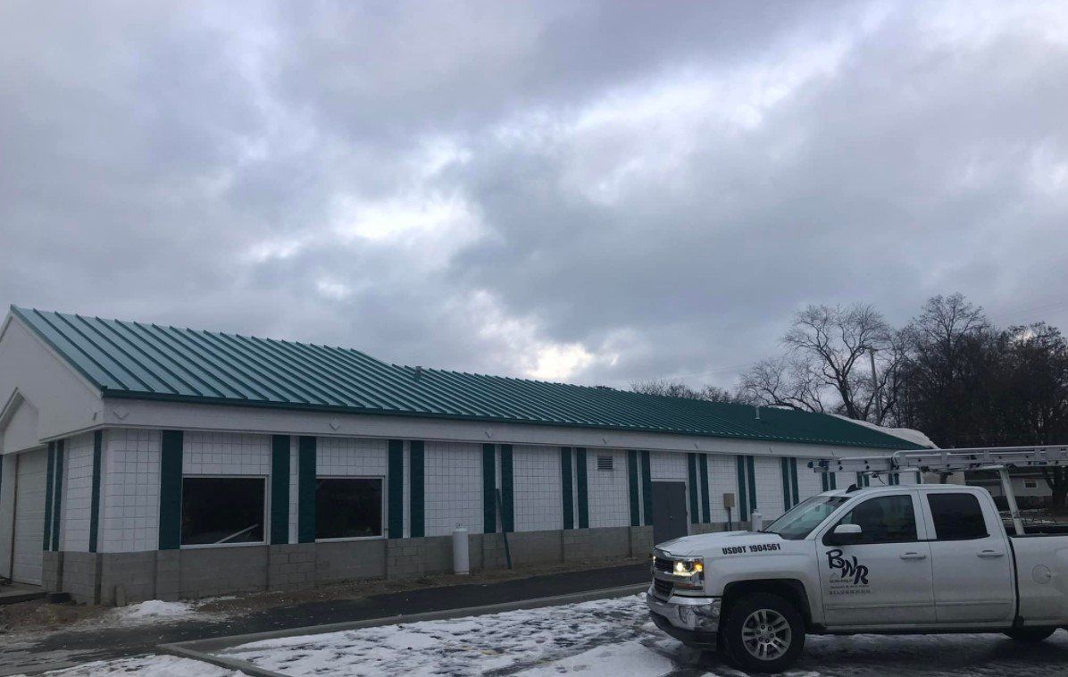 White pickup truck parked near a building with a green metal roof under a cloudy sky.