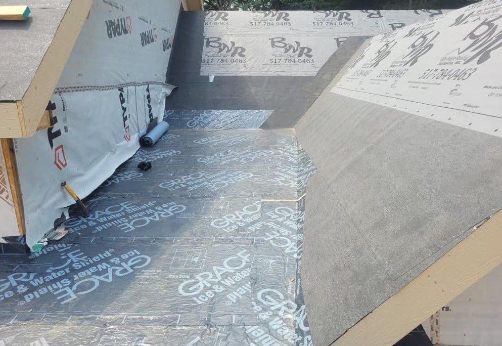 Roof under construction with black waterproof membrane and gray wood beams.