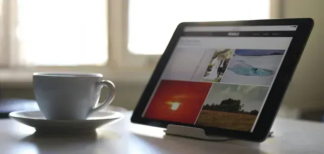 A tablet is sitting on a table next to a cup of coffee.