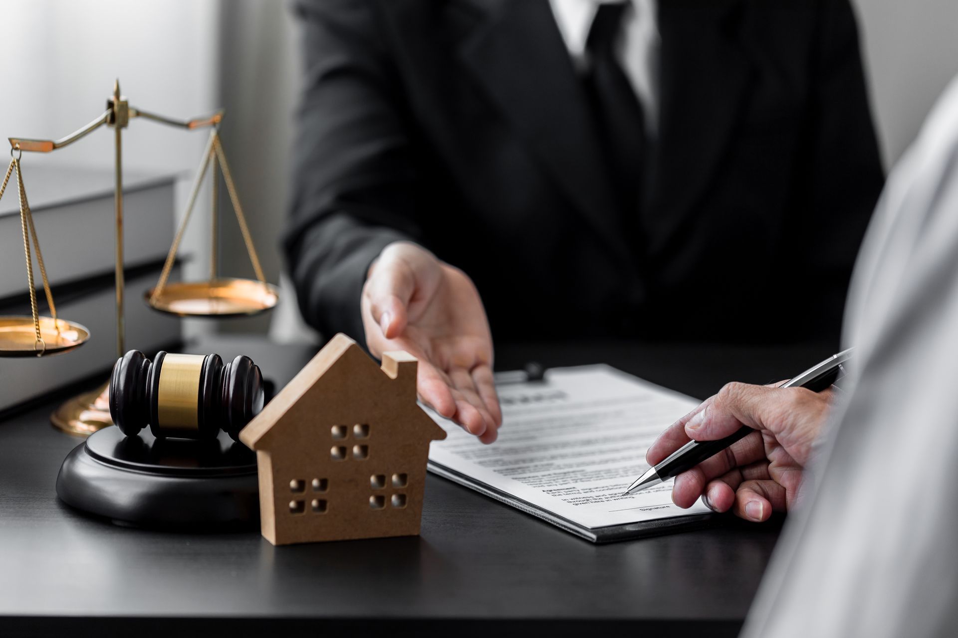 Lawyer discussing foreclosure papers beside a house model, gavel, and scales of justice
