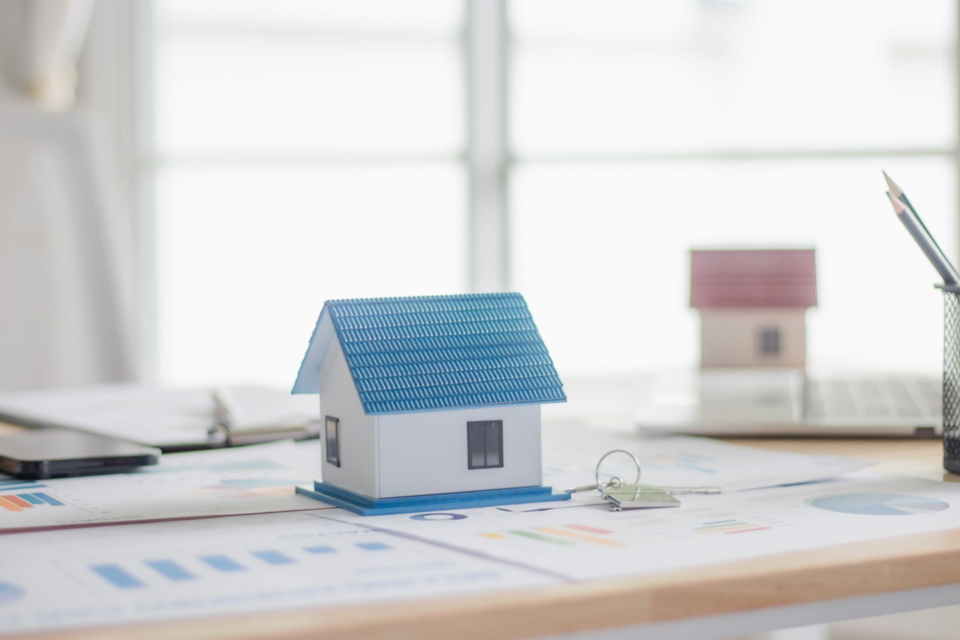 Small blue-roofed house model on architectural plans with another model and drafting tools in the background