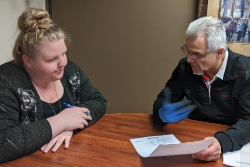 Two people discussing a paper at a wooden table indoors