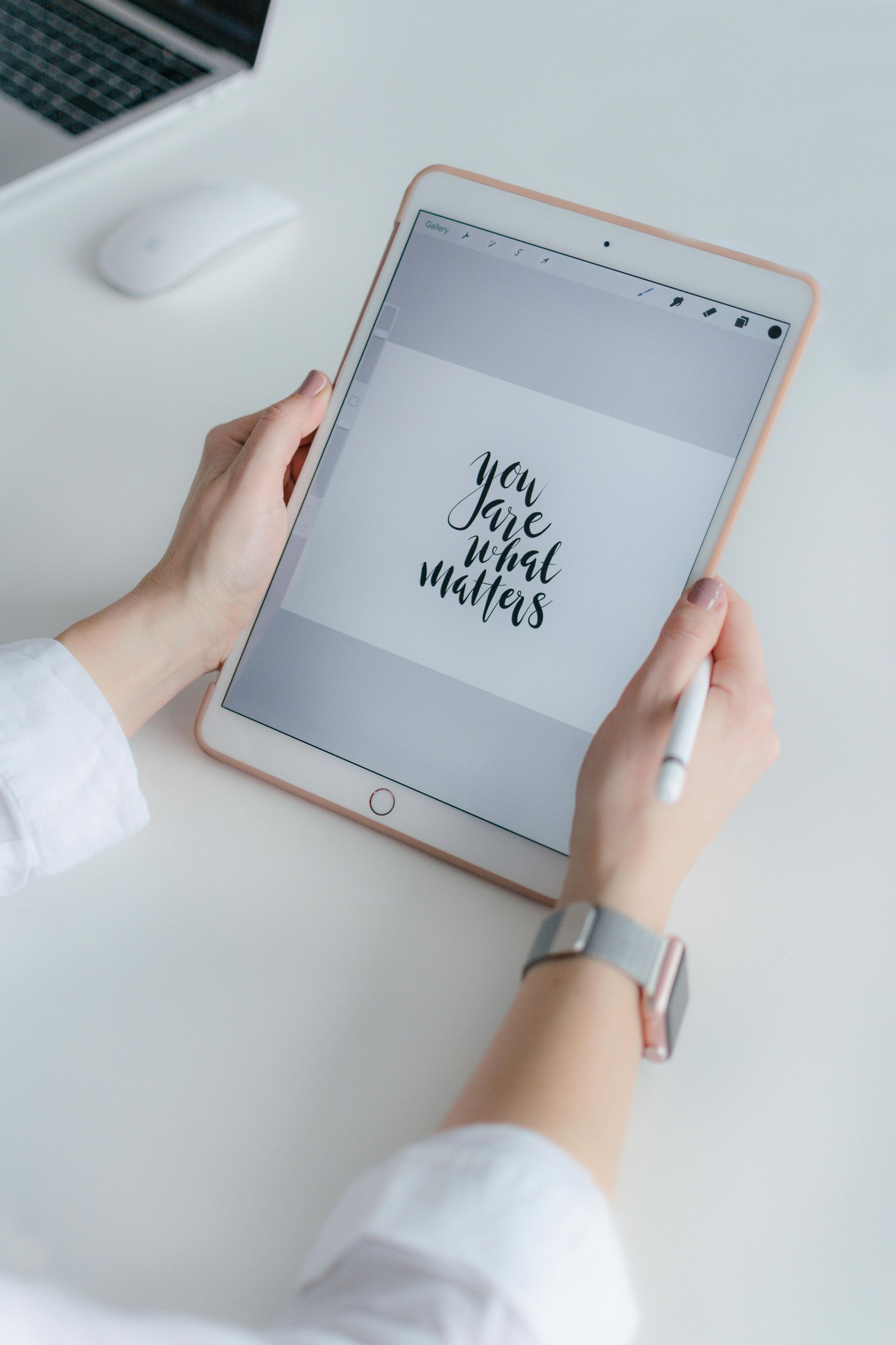 Person som håller en surfplatta med handstil, en styluspenna och en smartklocka på ett vitt skrivbord.