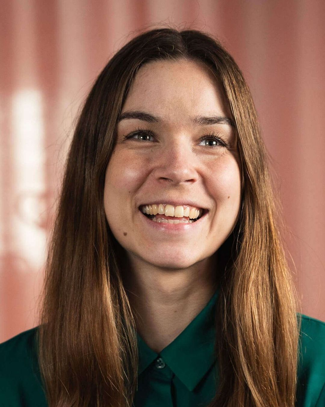 A woman with long hair is smiling and wearing a green shirt.