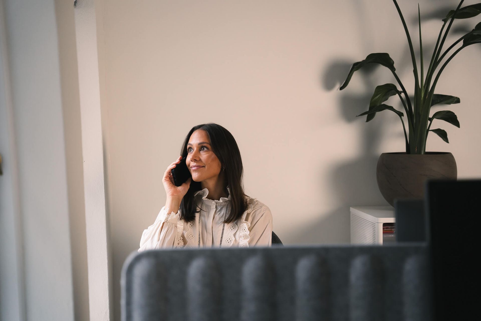 A woman is sitting at a desk talking on a cell phone.