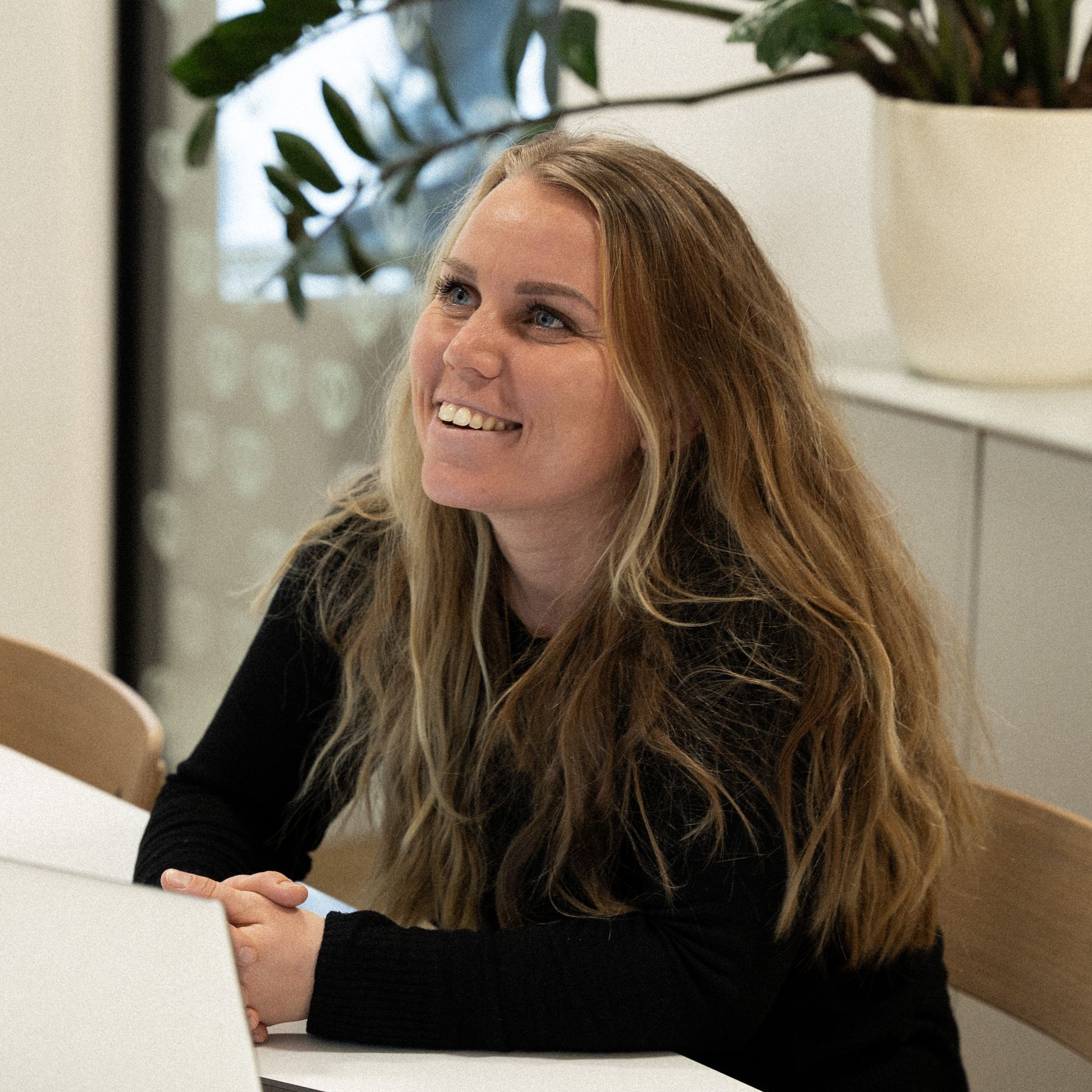 A woman is sitting at a table with a laptop and smiling