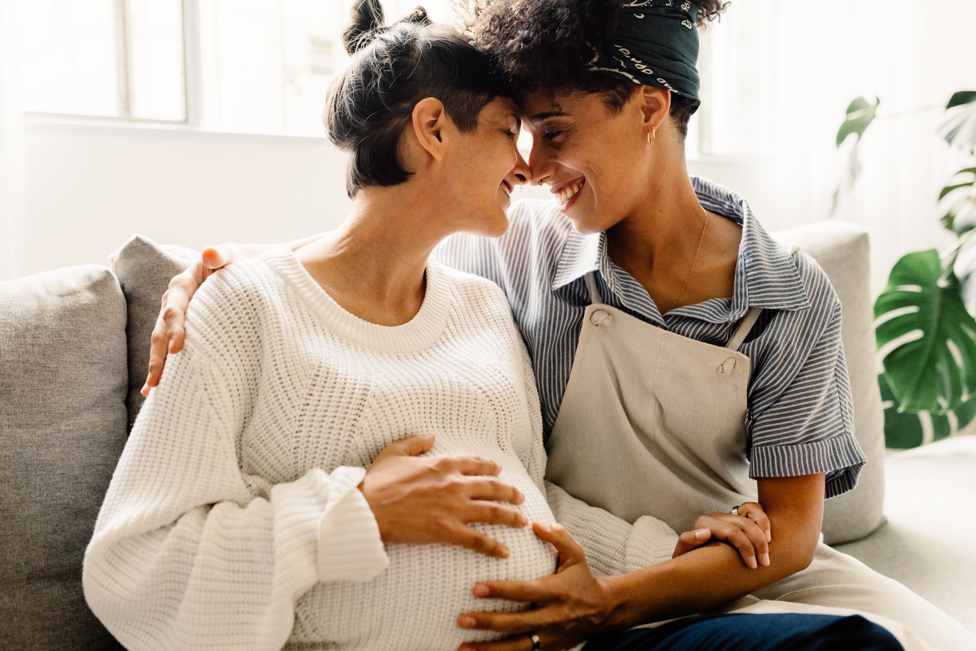 A pregnant woman is sitting on a couch with her partner also a woman.