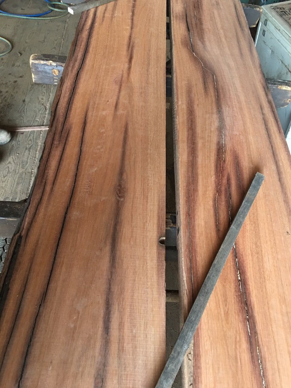 Two wood slabs with reddish-brown grain and dark streaks, possibly for a table top, with a file.