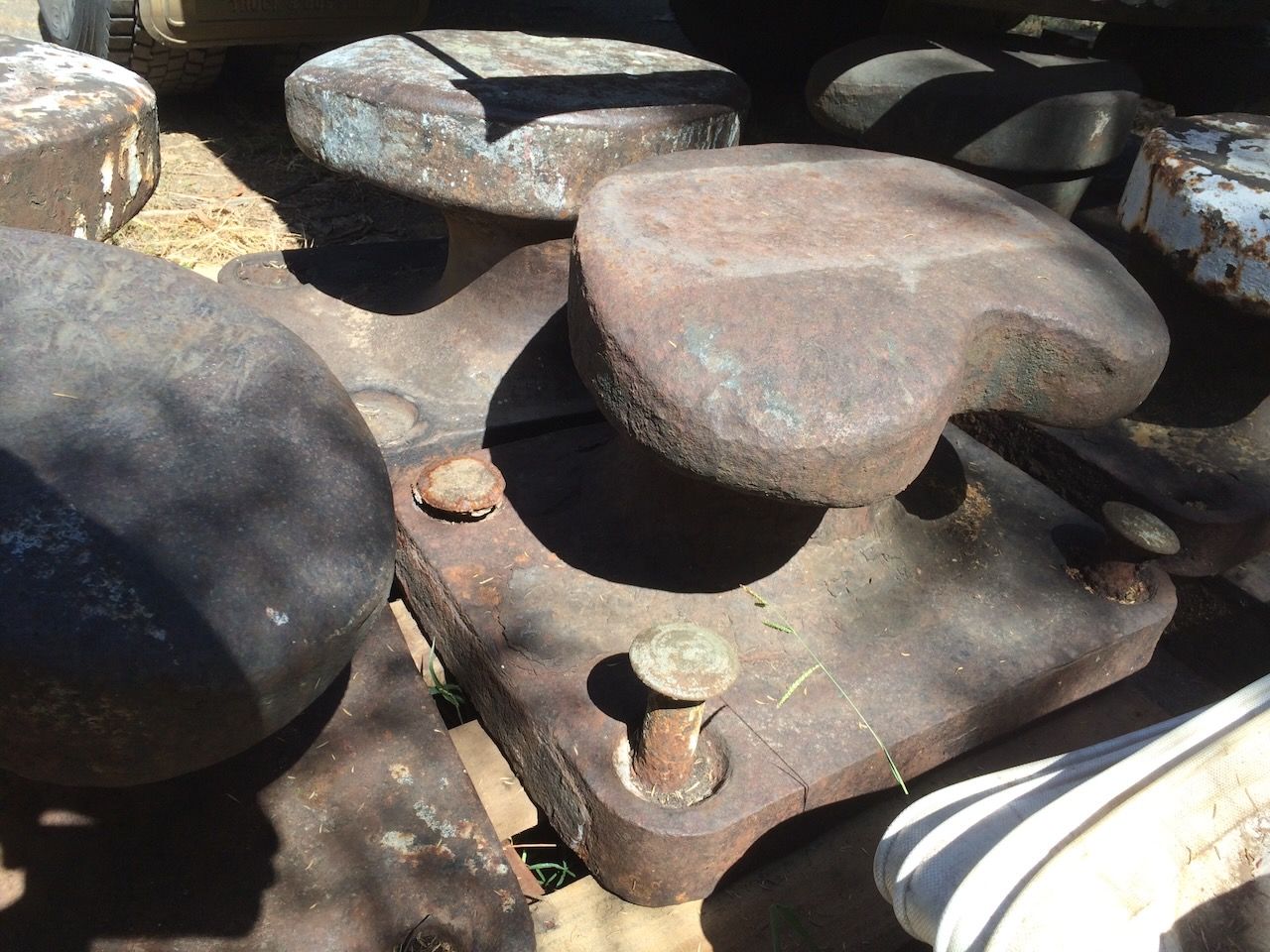 Weathered, rusty metal industrial parts stacked outdoors in sunlight.