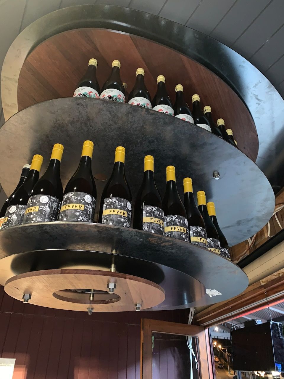 Bottles of wine displayed on a circular, tiered shelf with a wooden backing and silver exterior.