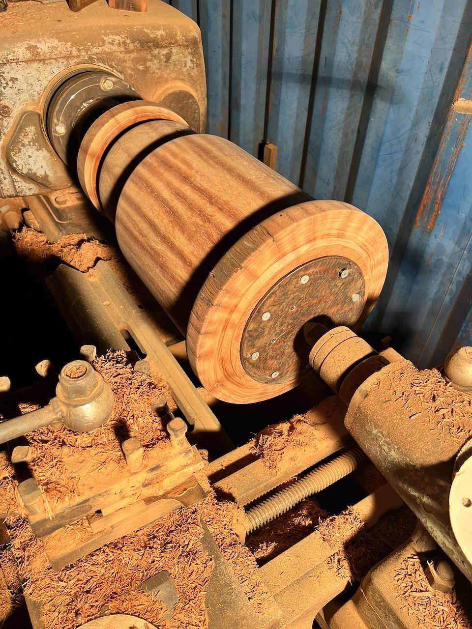 Wooden barrel being turned on a lathe, surrounded by wood shavings in a workshop setting.