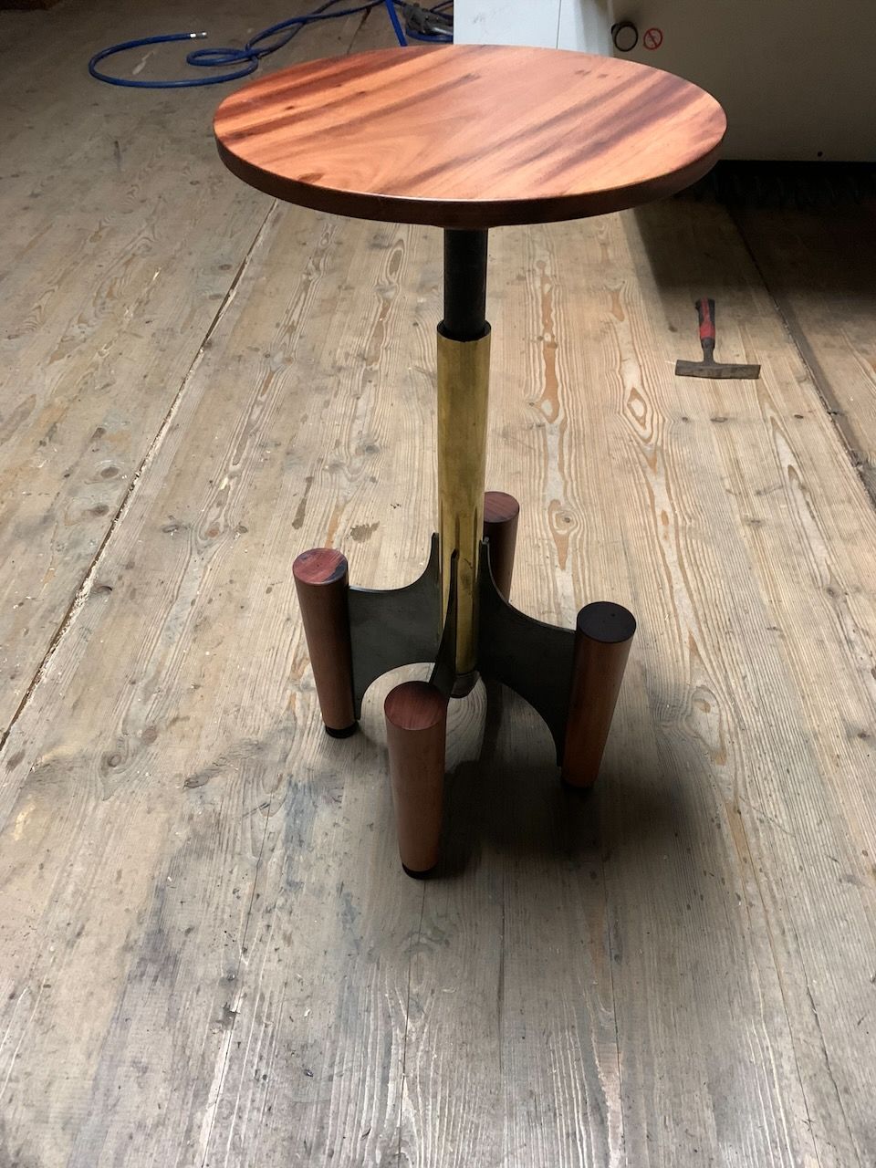 Round wooden table with three brown legs, on a wooden floor.