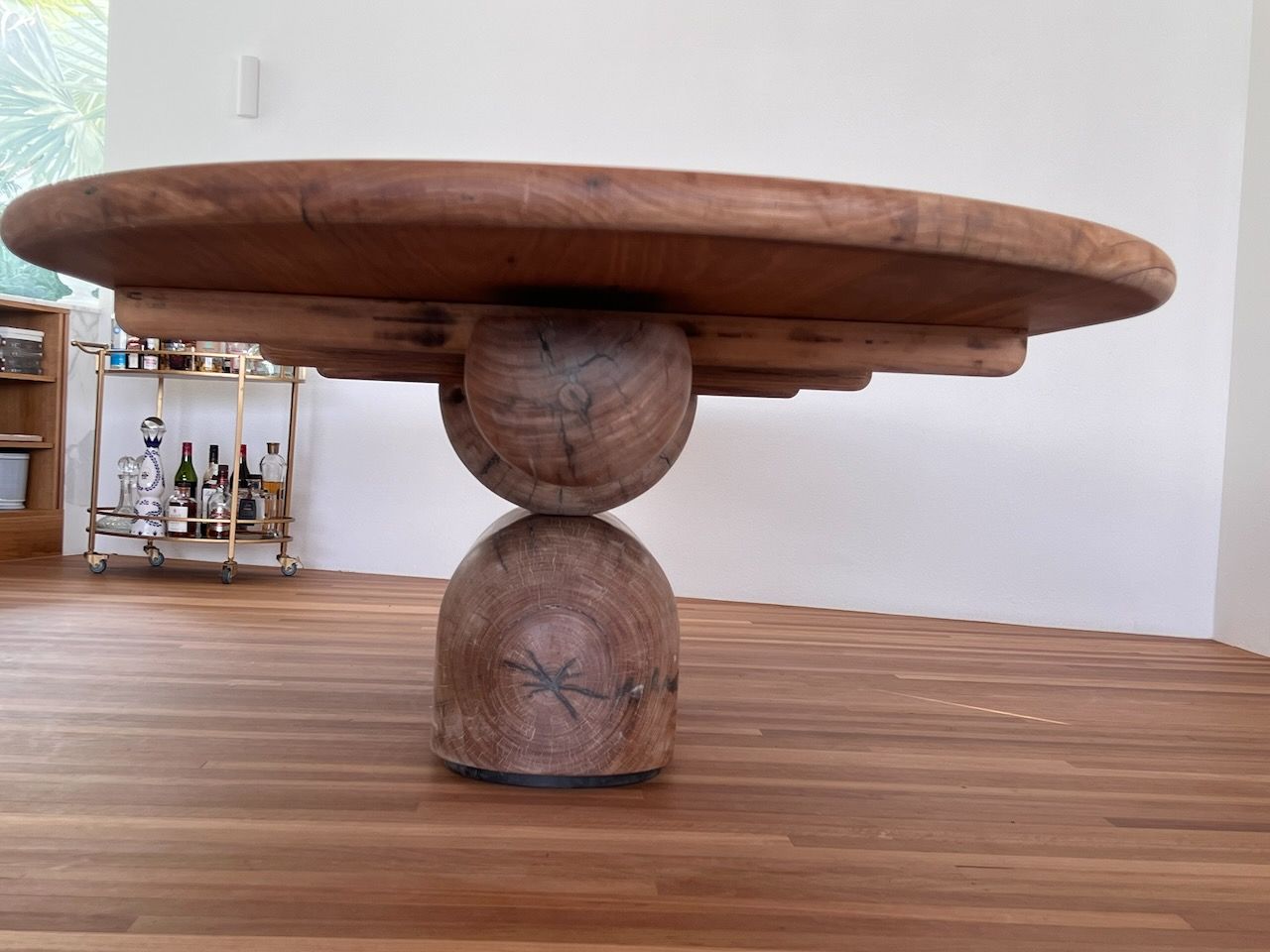 Round wooden dining table with a unique stacked sphere base on hardwood floor.