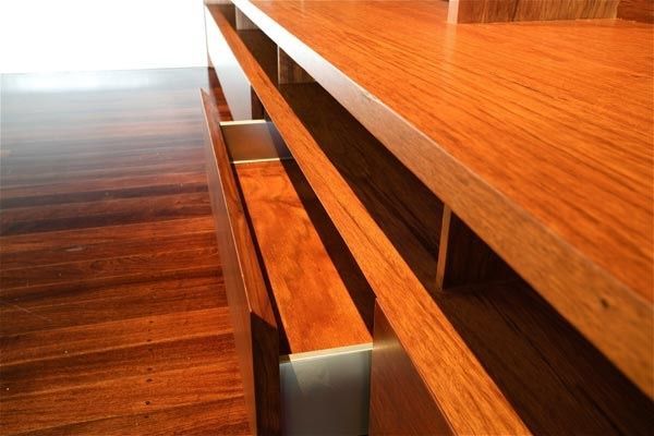A low-angle view of a sleek wooden cabinet with an open drawer against a dark wood floor.