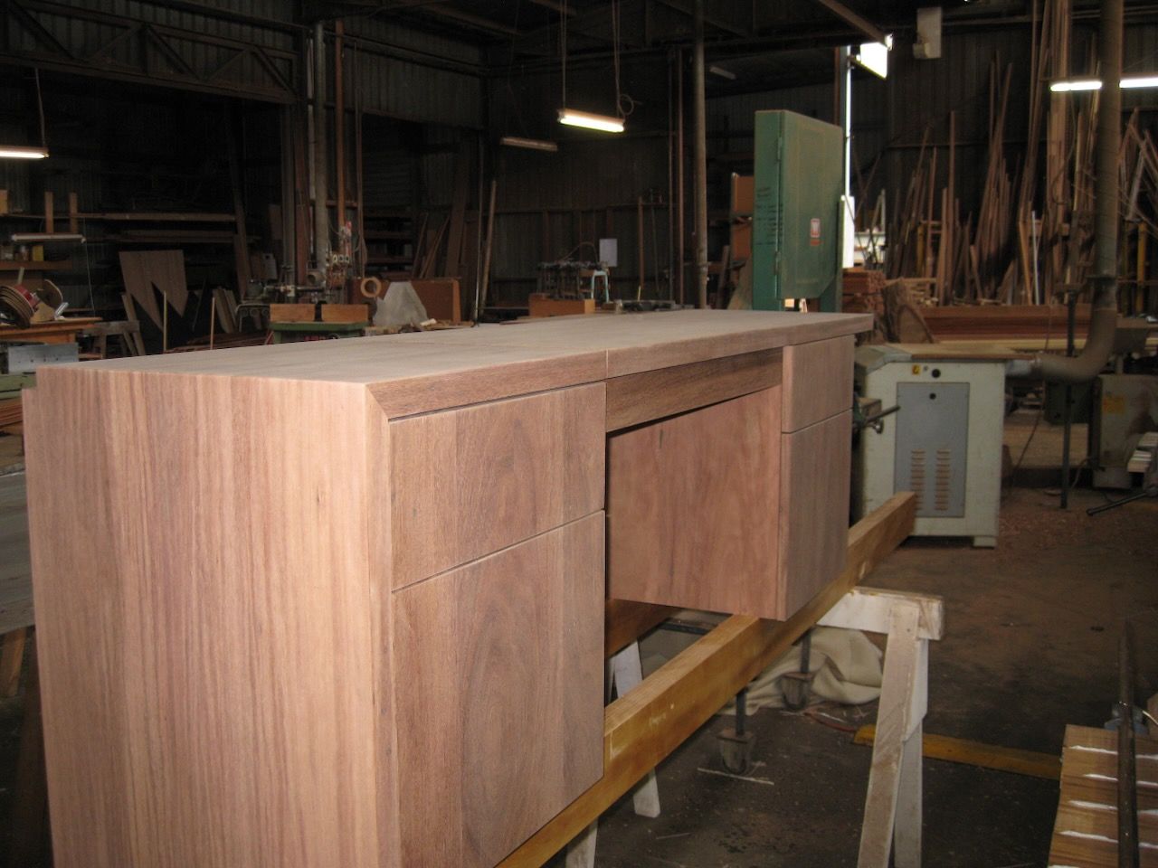 Wooden desk under construction in a wood workshop, resting on a sawhorse.