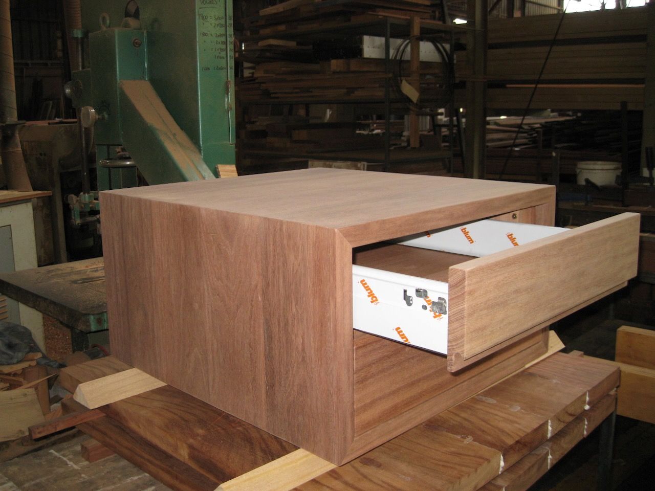 Wooden cabinet with a drawer pulled open, in a woodworking shop.