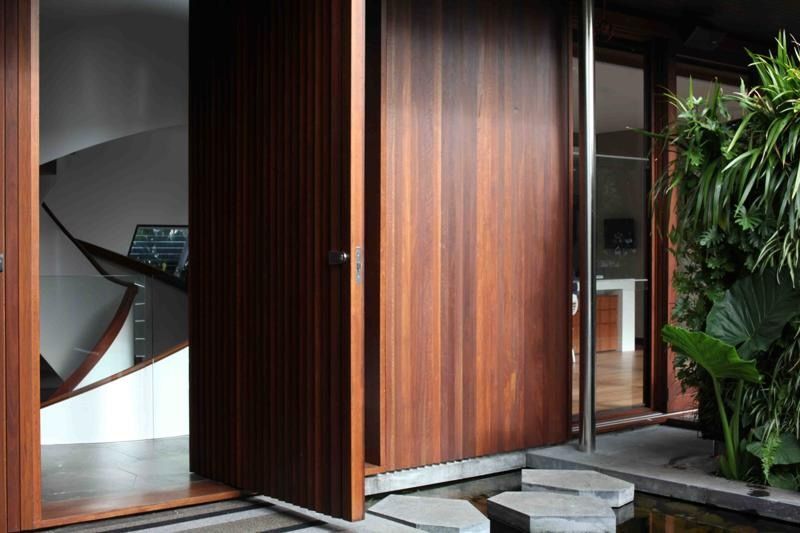 Large wooden pivot door, partially open. A staircase and green wall are visible beyond.