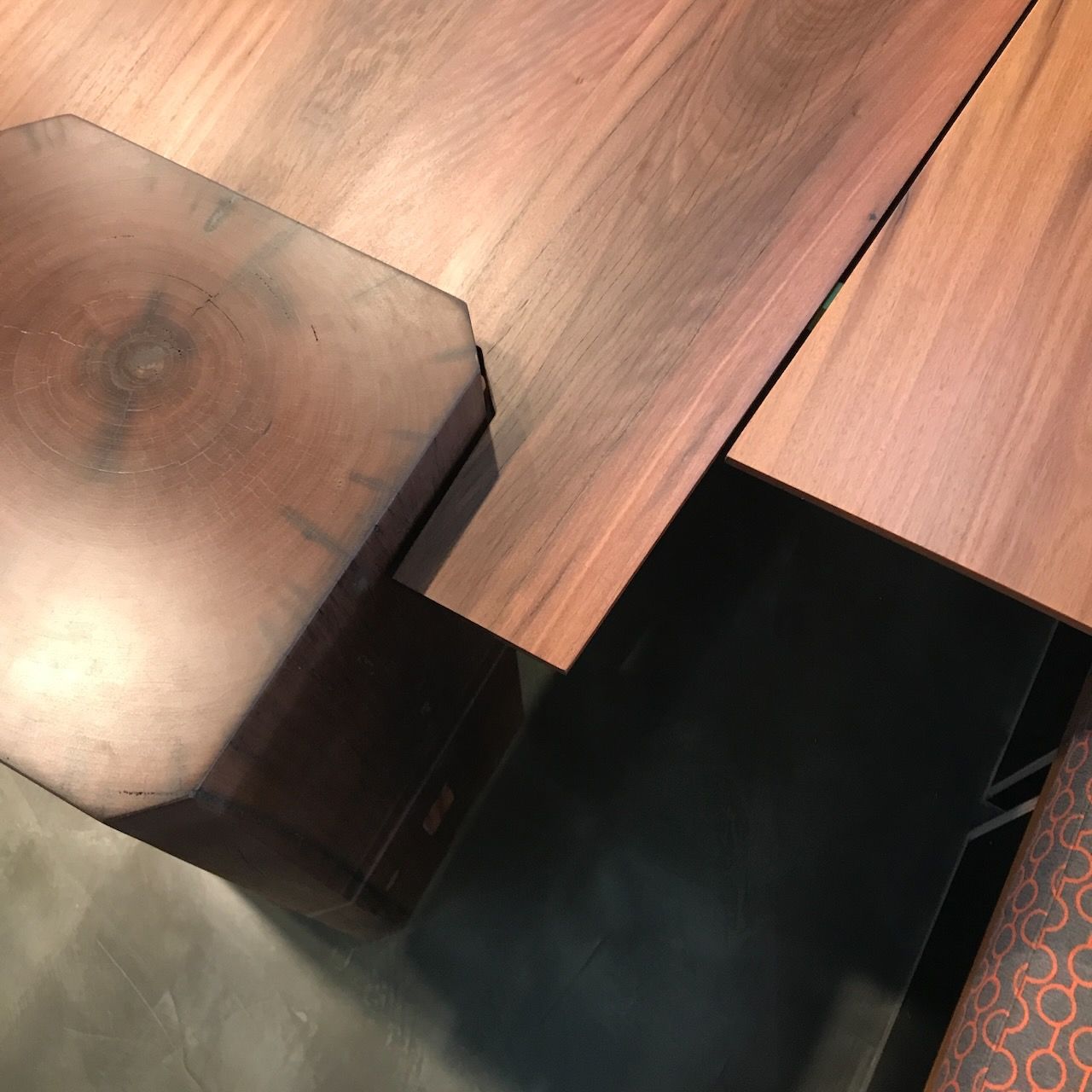 Top-down view of a dark wooden table with a thick, notched leg and a matching wood extension panel on a black base.