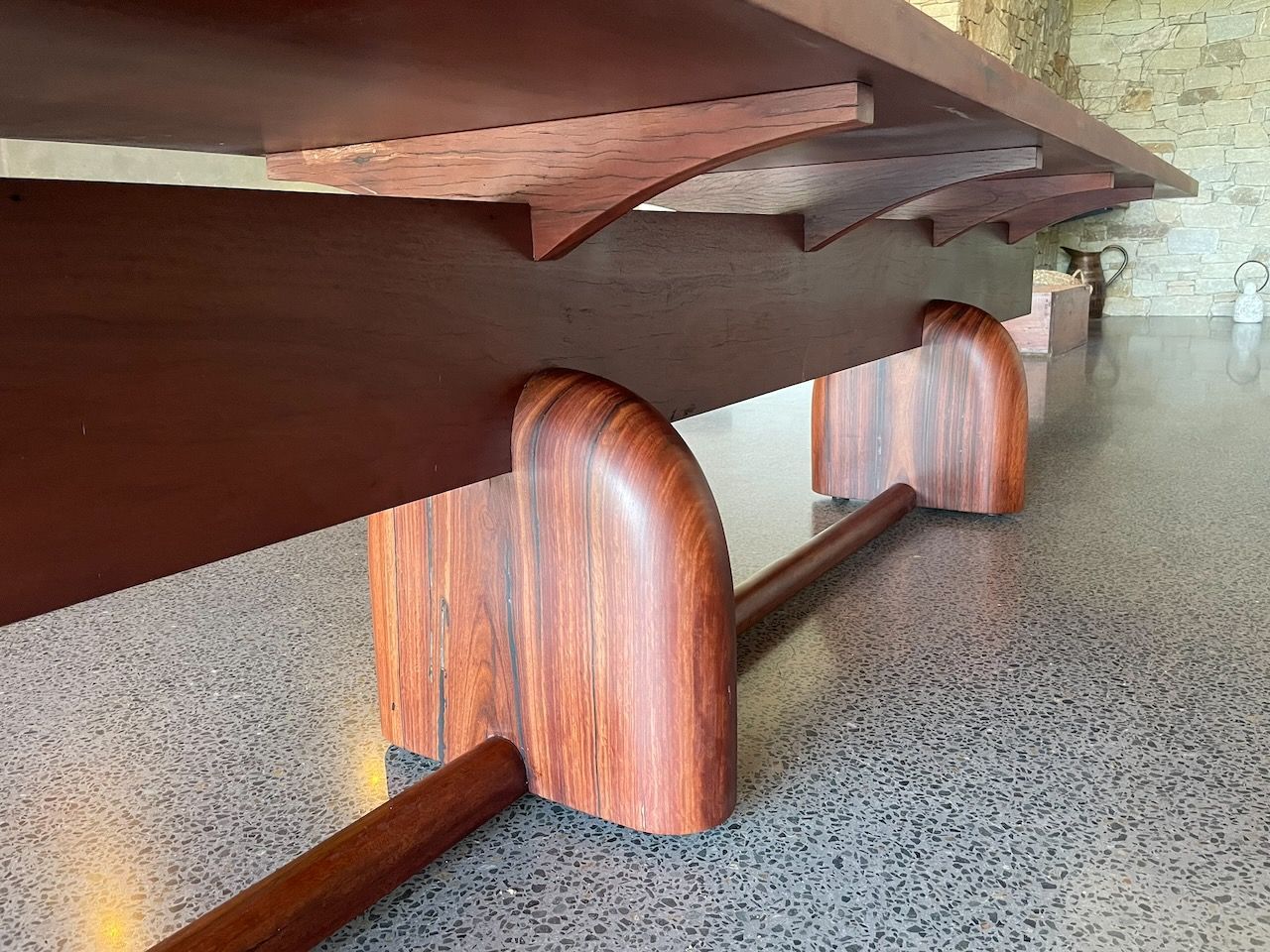 Close-up of a large, dark wooden table with curved supports and a stone wall background in Brisbane.