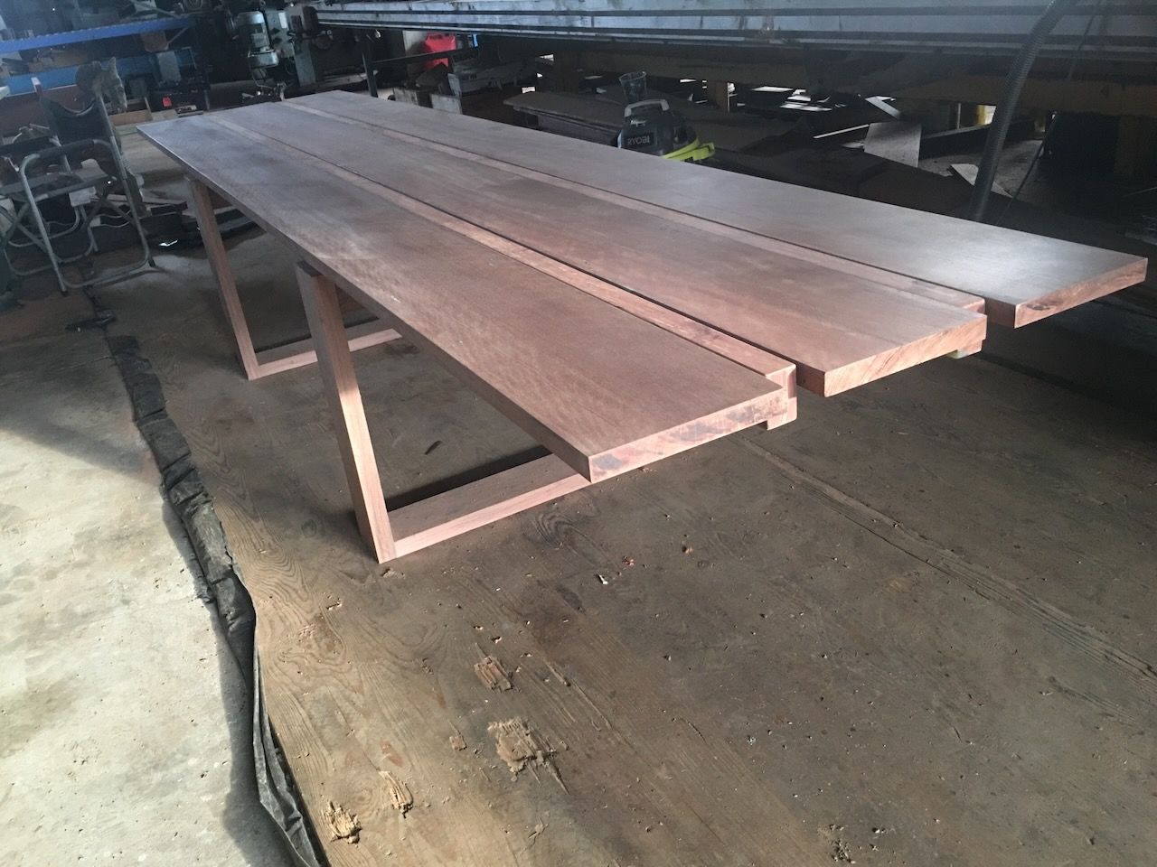 Wooden outdoor table with a dark reddish-brown surface and a geometric leg design, set in a workshop.