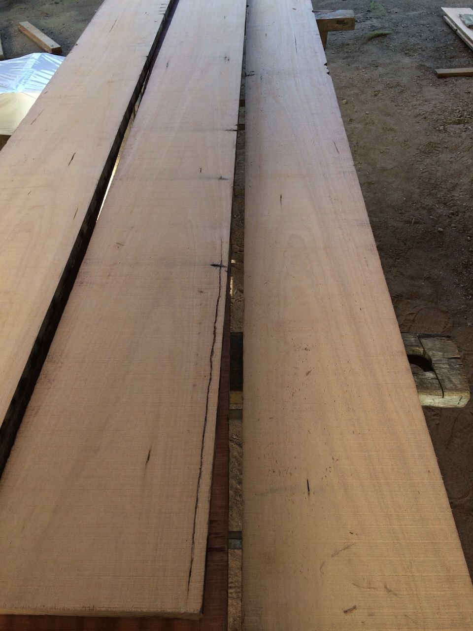 Three long, light-brown wooden boards lie side-by-side, indoors on a slightly rough surface.