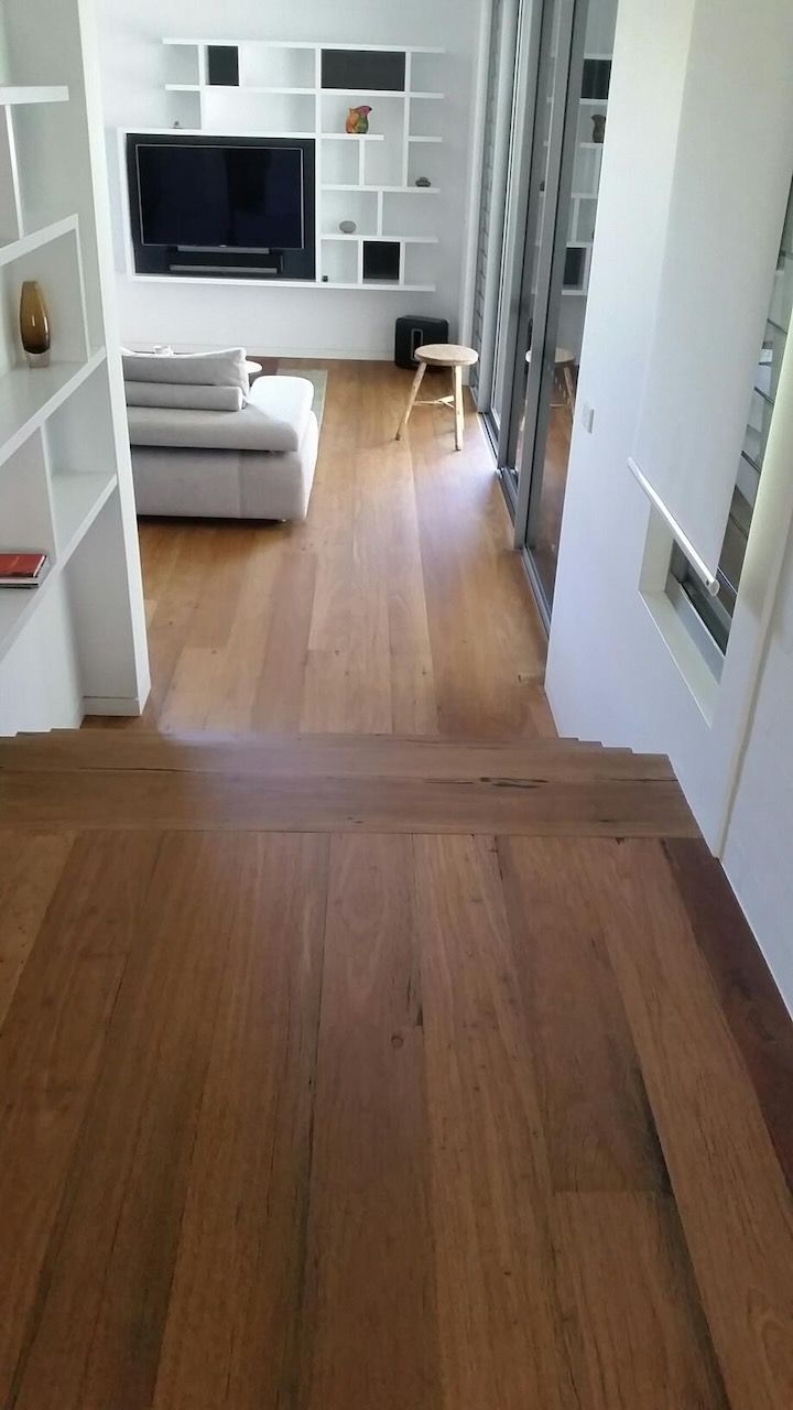 Wooden floor leading to a living room with white shelves, couch, and a TV.