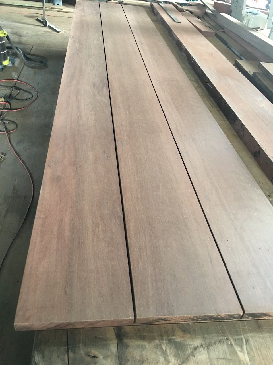 Long, reddish-brown wooden planks arranged side-by-side, possibly for a surface like a tabletop.