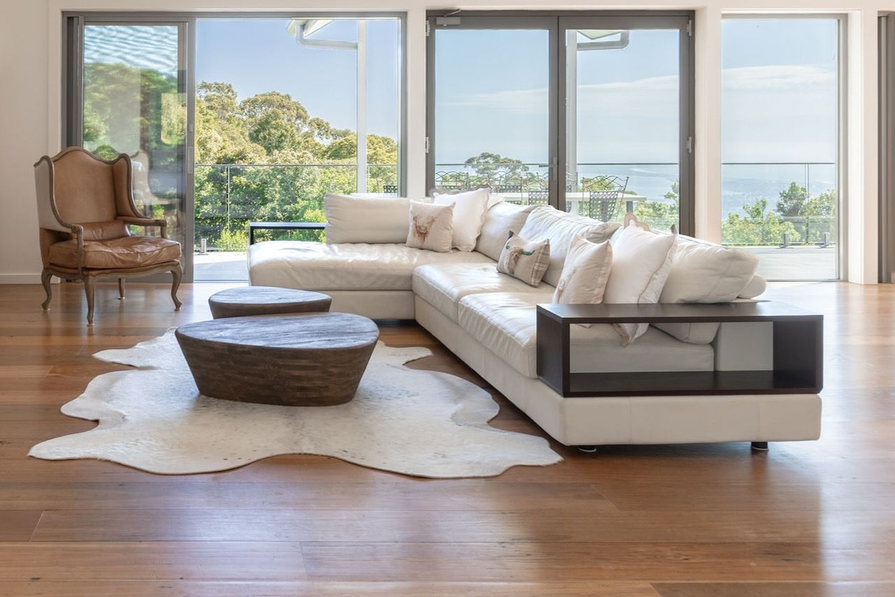 Living room with white sectional sofa, cowhide rug, coffee tables, and large windows with a view in Brisbane.