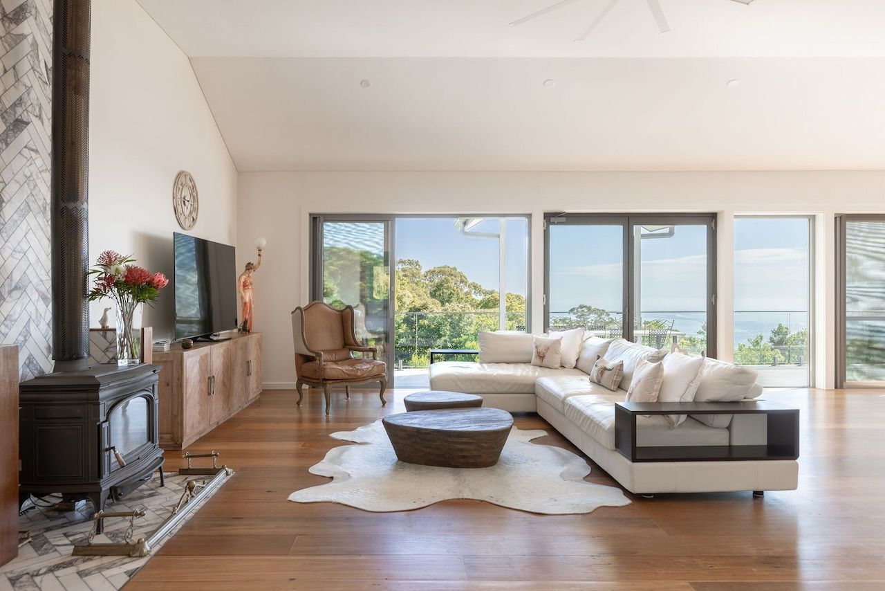 Spacious living room with white sectional sofa, wood floors, large windows with a view, and a wood-burning stove.
