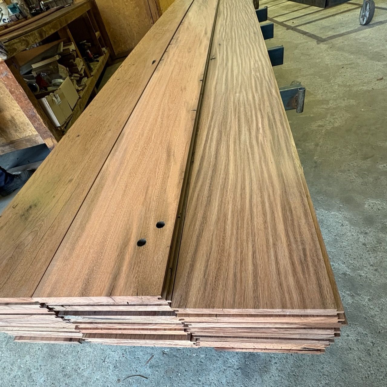 Pile of reddish-brown wood planks, stacked and arranged in a workshop setting in Brisbane.