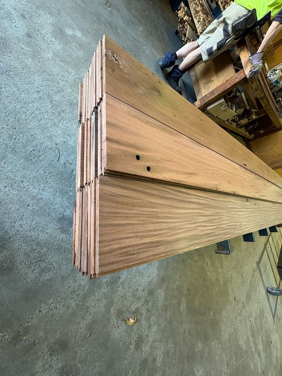 Stack of brown wooden planks on a concrete floor, viewed from a high angle.