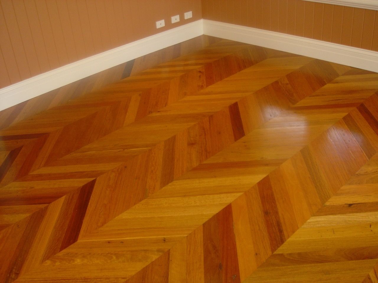 Hardwood floor with a diagonal chevron pattern, set in a corner of a room.