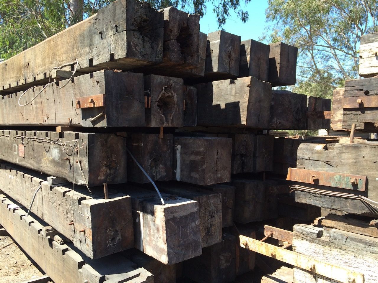 Stack of weathered, rectangular wooden railway sleepers with rusty metal hardware outdoors in Brisbane.