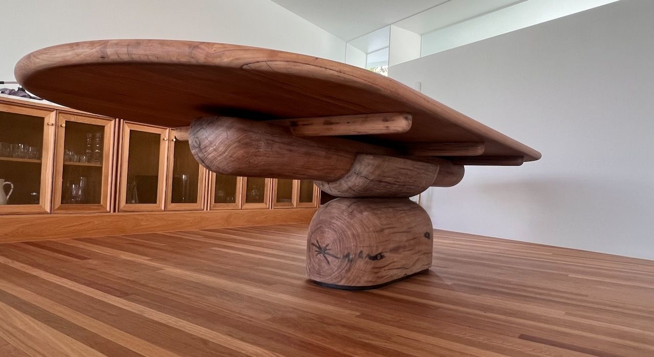 Wooden table with a sculptural base, set on a wood floor in a room in Brisbane.