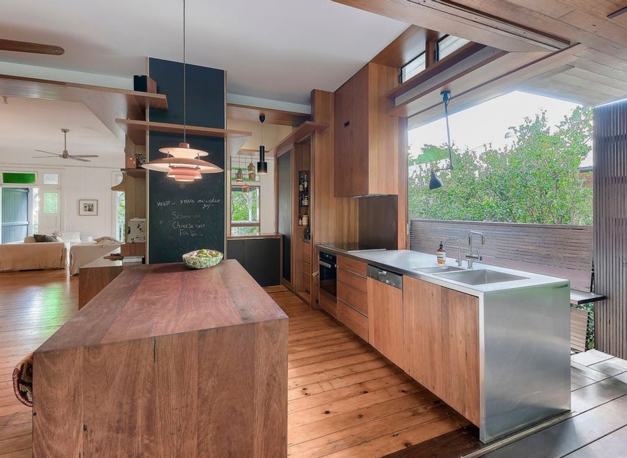 A modern kitchen features a large wooden island, wood cabinetry, a stainless steel sink, and a chalkboard wall.