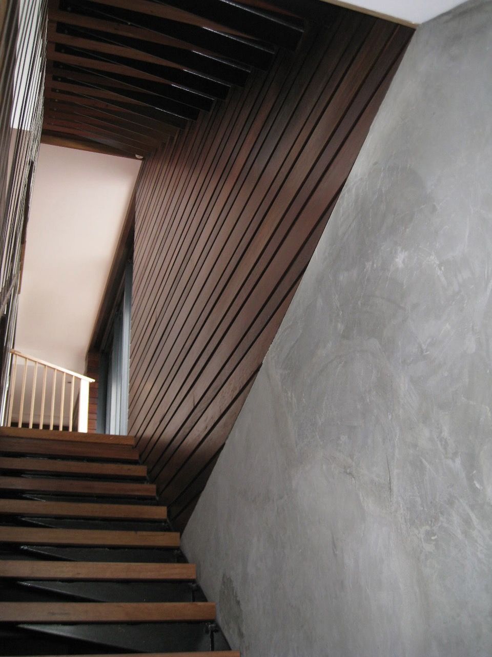 Staircase with wooden steps and walls. Angled, dark wooden paneling on one side, concrete wall on the other in Brisbane.