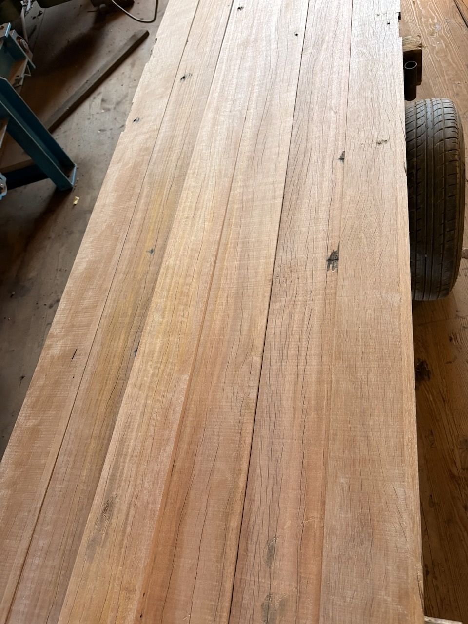 Wooden planks, reddish-brown color, stacked on a surface, next to a tire in Brisbane.
