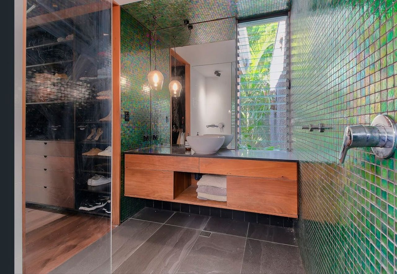 Bathroom with green mosaic tiles, wood vanity, and a large window looking onto greenery.