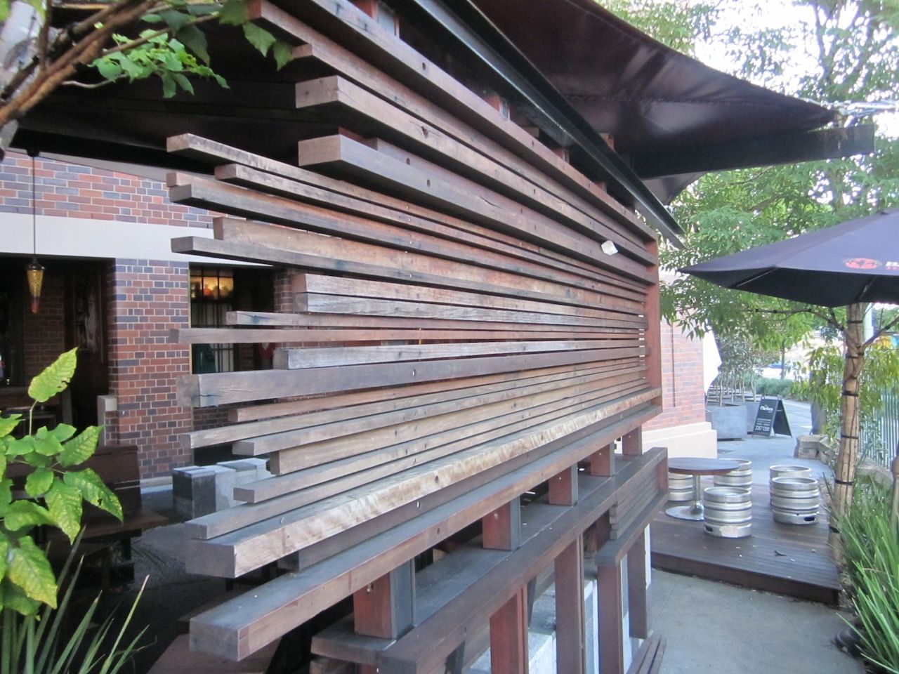 Wooden planks create a textured wall on a building's exterior.  A nearby patio has umbrellas and kegs in Brisbane.