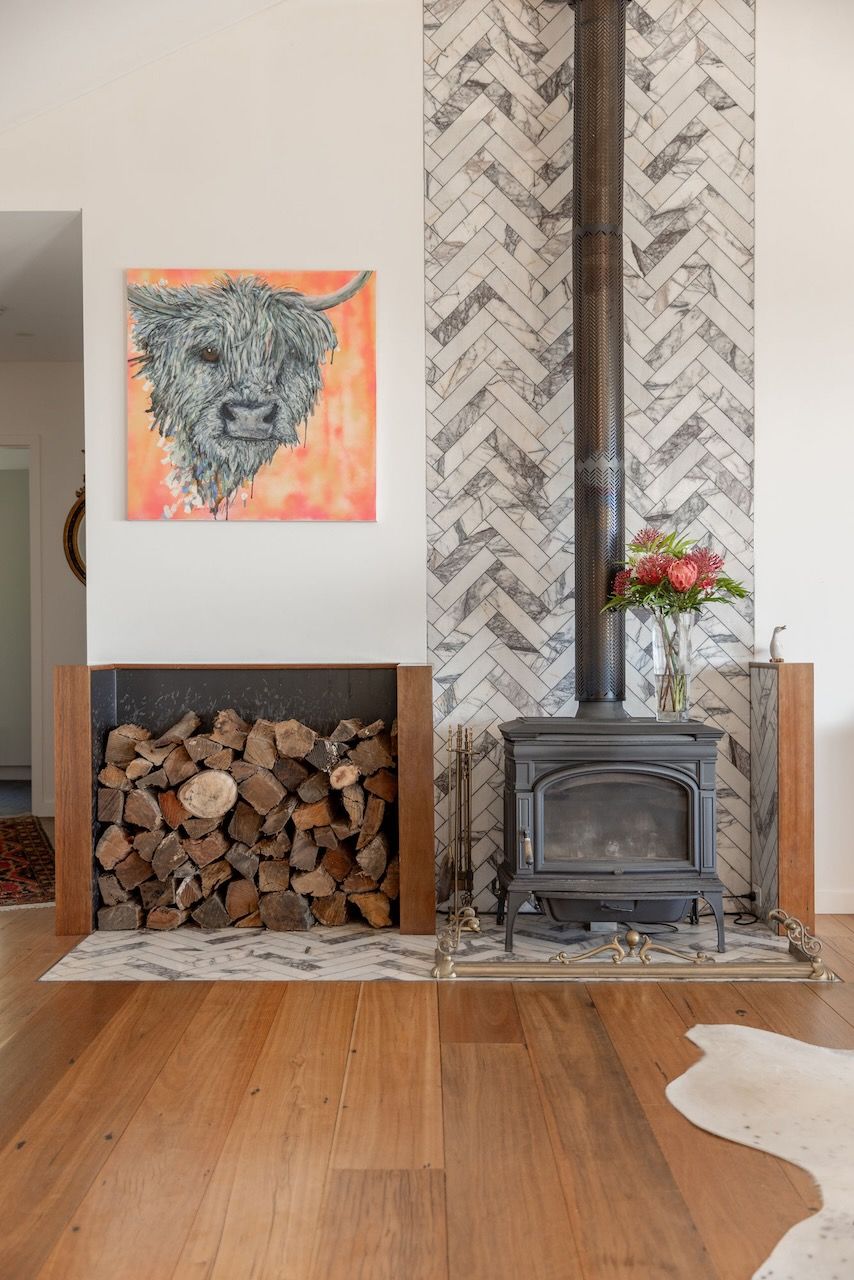 Fireplace with wood storage, wood-burning stove, marble herringbone background, artwork, and hardwood floor.